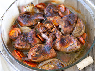 Delicious fried Quails with vegetables - garlic, carrots, onions , baked in a glass form with a rustic wooden background. Dietary, gourmet lunch. Close up, selective focus.