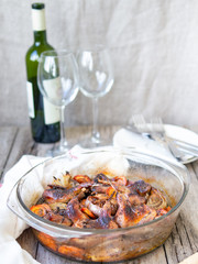 Delicious fried Quails with vegetables - garlic, carrots, onions , baked in a glass form, bottle of white wine and two glasses on a rustic wooden background. Dietary, gourmet lunch. Close up.