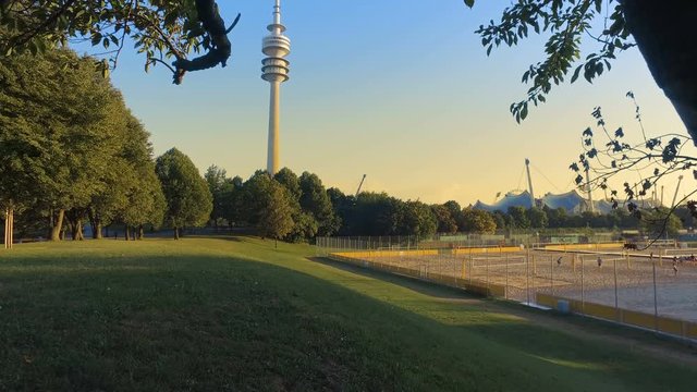 The Olympic Tower (Olympiaturm) in the Olympic Park (Olympiapark), view among the tree branches eat sunset, Munich, Germany
