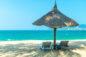 Two loungers under strawy parasol on sandy beach