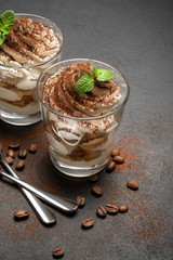 two portions Classic tiramisu dessert in a glass on dark concrete background