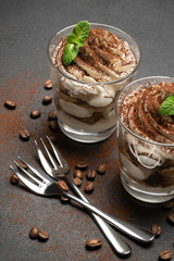 two portions Classic tiramisu dessert in a glass on dark concrete background
