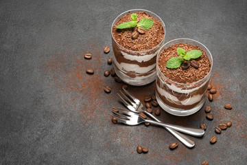 two portions Classic tiramisu dessert in a glass on dark concrete background