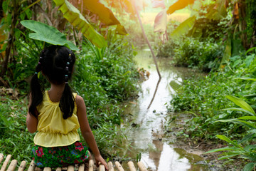 A little girl dressed in a Thai dress holding a bonbon leaf, sitting on a bamboo floor along the...