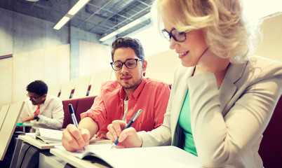 Obraz premium education, high school, university, learning and people concept - group of international students with notebooks writing at lecture hall