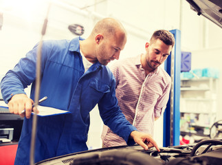 auto service, repair, maintenance and people concept - mechanic with clipboard and man or owner looking at broken car engine at shop