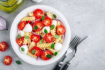 Italian pasta salad with tomatoes, mozzarella cheese, red onion and basil. Top view.