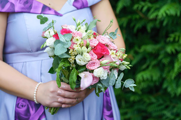 Obraz na płótnie Canvas Caucasian female guest or bridesmaid wearing a lilac summer dress which shows a lovely baby bump and holding a delicate free-form bouquet featuring different color roses, pink callas and greenery