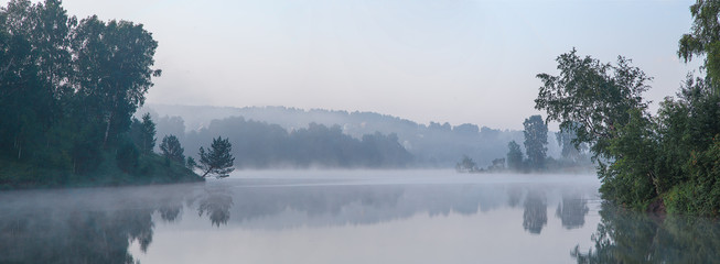 Early foggy morning on a lake in Siberia with beautifully hanging trees above the water.