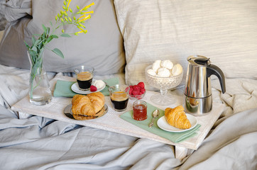 Romantic Breakfast  or brunch for two in bed. Coffee maker  and coffee glasses, croissants, jam, berries, meringue and flowers on wood tray. Romantic good morning scenery