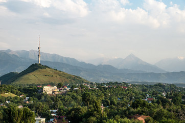 The view from the city of Almaty to the high television tower on a small hill. In the background you can see high peaks of mountains and rocks.