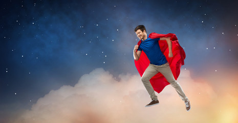 super power and people concept - happy young man in red superhero cape flying in air over starry night sky background