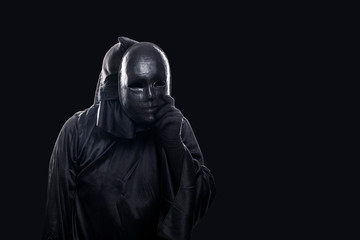 Fototapeta na wymiar Scary figure in hooded cloak with mask in hand isolated on black background
