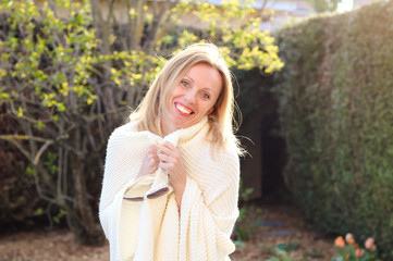 Happy attractive joyful blond girl in ivory knitted plaid smiling and looking at camera outdoors in garden at fresh sunny evening. Lifestyle