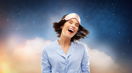people and bedtime concept - happy young woman in pajama and eye sleeping mask over starry night...
