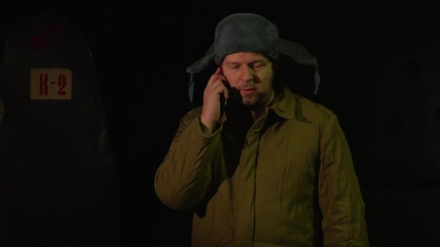 Russian man in a hat with earflaps, talking on the phone in a dark basement and decides matters of national importance.
