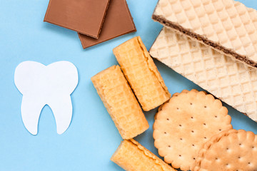Tooth and sweets on blue background. Sugar destroys tooth enamel and leads to tooth decay. Caries concept.