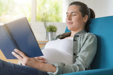 Pregnant woman in armchair reading a book and relaxing