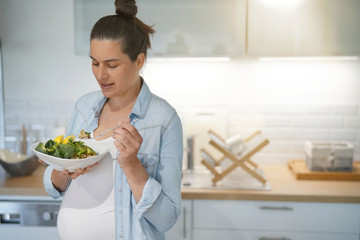 Pregnant woman in home kitchen eating healthy salad