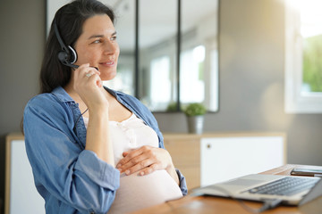 Pregnant woman working from home with laptop and headset
