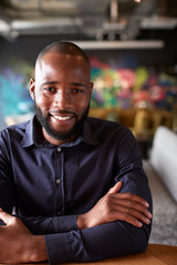 Obraz premium Mid adult black male creative sitting at a table in an office cafe smiling to camera, close up, crop