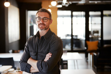 Middle aged white male creative wearing glasses standing in an office looking to camera, waist up