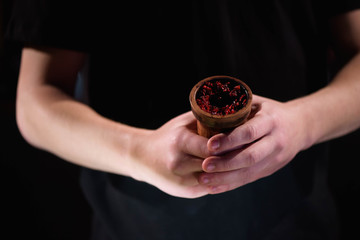 Barman fills black burnt ceramic bowl for hookah smoking different types of tobacco.