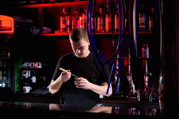 Barman fills black burnt ceramic bowl for hookah smoking different types of tobacco.