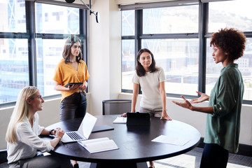 Female creatives in a meeting room listening to their colleague making an informal presentation