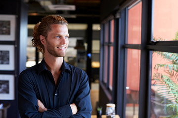 Millennial white male business creative smiling and looking out of the window in an office, waist up