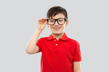 school, education and vision concept - portrait of smiling little boy in red polo t-shirt in glasses over grey background