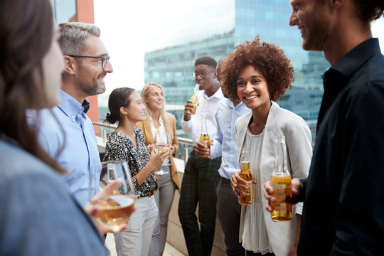 Business colleagues talking and drinking together on a balcony in the city after work