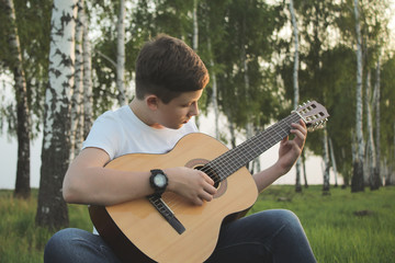 teenager playing guitar outdoors in the summer on the background of birch trees.