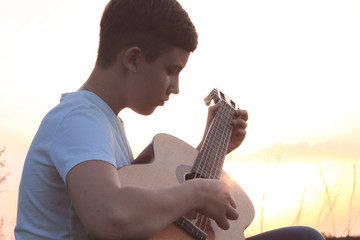 teen playing guitar outdoors in the summer on the background of birch trees.