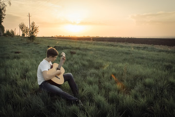 teen playing guitar outdoors in the summer on the background of birch trees.
