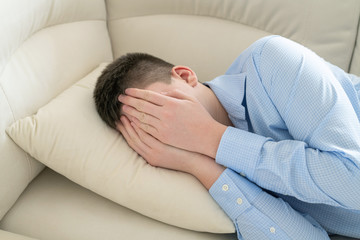 Depressed teenager lying on couch covering his face with his hands