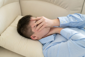 Depressed teenager lying on couch covering his face with his hands