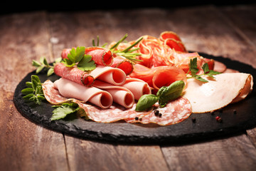 Fototapeta na wymiar Food tray with delicious salami, pieces of sliced ham, sausages,salad and vegetable. Meat platter with selection