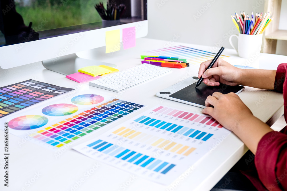 Poster Image of female creative graphic designer working on color selection and drawing on graphics tablet at workplace