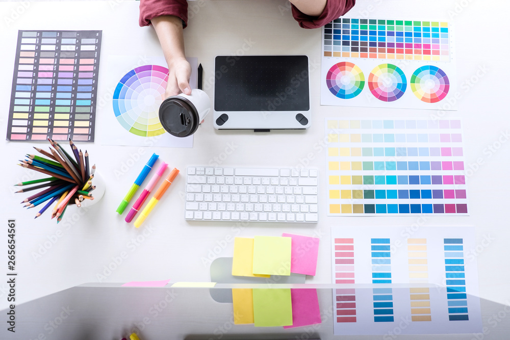Poster Image of female creative graphic designer working on color selection and drawing on graphics tablet at workplace, top view workspace