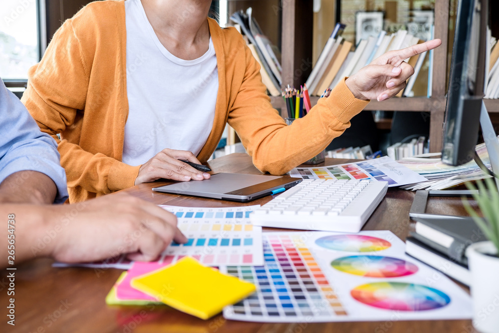 Poster Two colleague creative graphic designer working on color selection and color swatches, drawing on graphics tablet at workplace with work tools and accessories