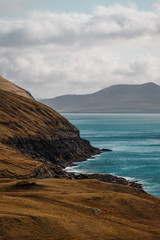 Coastal cliffs with turquoise Atlantic water near the small village of Norðradalur on a windy spring afternoon (Faroe Islands, Denmark, Europe)