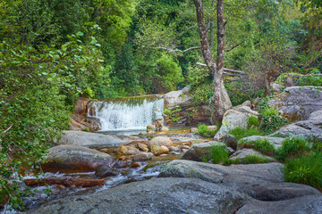 Fisherman in the water fishing trout near a waterfall on the river in spring