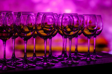 Stemware in purple light. Many glass of wine on a table. Glasses with wine. Filled with half and stand on the holiday table. Furshet. selective focus
