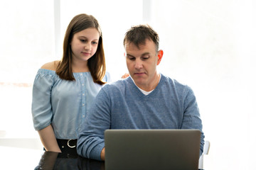 A father using a laptop in kitchen with teenager