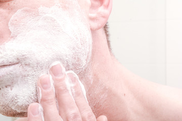 Applying shaving foam to face before shaving in the bathroom