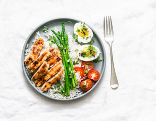 Balanced healthy lunch - rice, asparagus, grilled chicken, boiled egg on a light background, top view