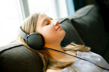 Girl listening music with headphones lying on couch at home