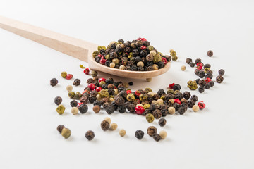 colored pepper peppercorns on wooden spoon on white background