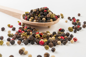 colored pepper peppercorns on wooden spoon on white background